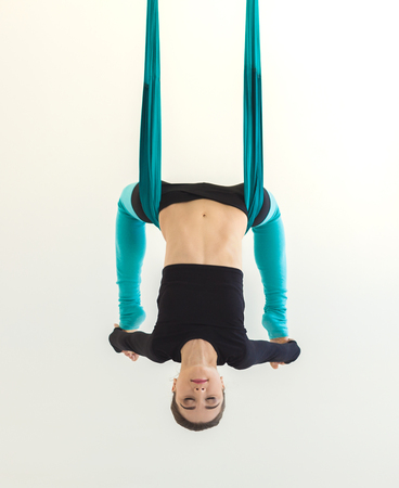 Young slim woman practicing fly yoga asana and stretching over white background in fitness gym, copy space, crop. Health, sport, yoga conceptの写真素材