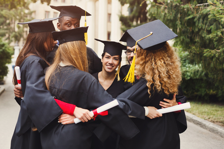 Group of multietnic students hugging on their graduation day at university, copy space. Education, qualification and gown concept.の写真素材