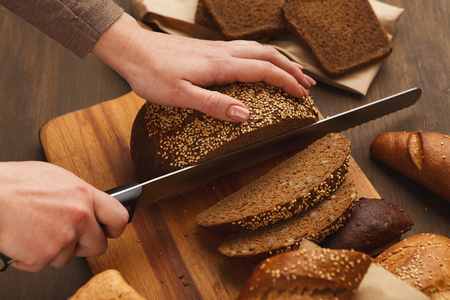 Cutting bread on wooden board. Unrecognizable female chef preparing healthy sandwiches, top view, copy spaceの写真素材