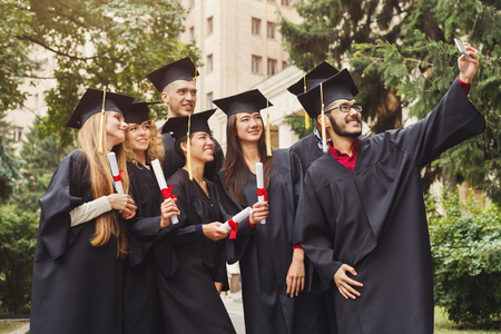 Group of multiethnic students taking selfie on smartphone to celebrate their graduation. Education, qualification and gown concept.の写真素材