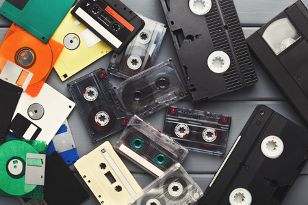 Retro media storage devices on gray wooden background. Audio and video cassettes and floppy discs, top view. Outdate technology conceptの写真素材