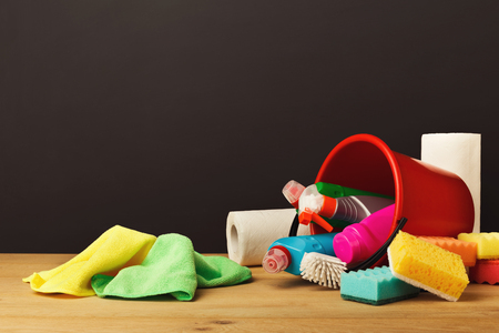 Variety of house cleaning products on wood table at black background. Pail, brush, colourful sponges and rags, disinfection products and other. Tidying up, spring-cleaning concept, copy spaceの写真素材