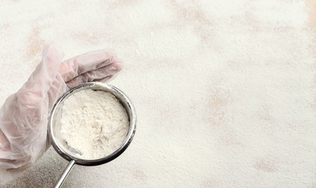 Male hand sifting flour from sieve on white kitchen table. Process of cooking pastryの写真素材