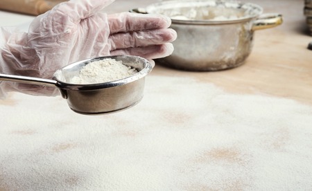 Male hands sifting flour from sieve on wooden kitchen table. Process of cooking pastryの写真素材