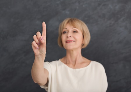 Middle aged woman pointing on invisible object on grey background, selective focusの写真素材