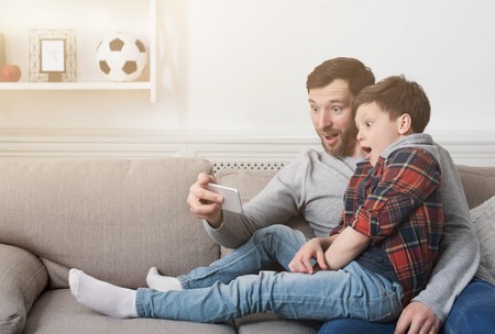 Funny father and his son taking selfie photo with smartphone at homeの写真素材