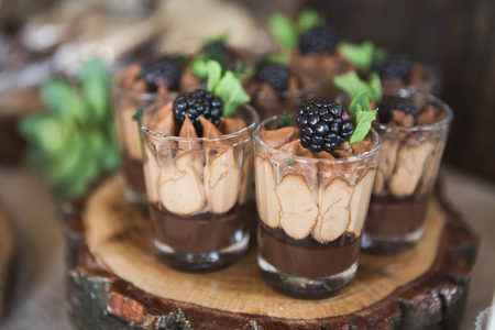 Chocolate dessert topped with cream, blackberry and mint in glass on wooden trayの写真素材