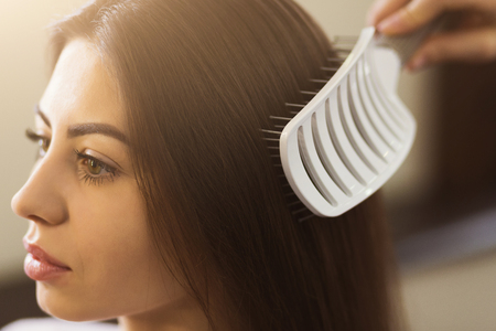 Stylist hand with comb combing woman hair at salonの写真素材