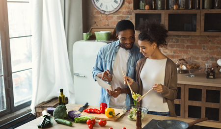 Black couple using digital tablet with recipe while preparing dinner in loft kitchenの写真素材