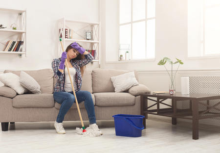 Young woman tired of spring cleaning house, resting on sofa after washing floor with mop, copy spaceの写真素材