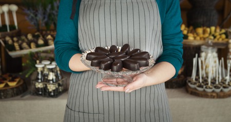 Female chef in apron holding plate with tasty chocolate sweets fir candy bar
