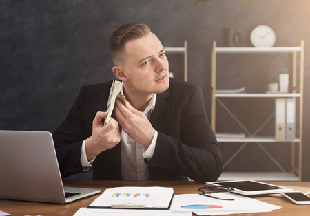 Businessman holding stack of money and listening to its sound. Counding bills on hear, profit or bonus, copy spaceの写真素材