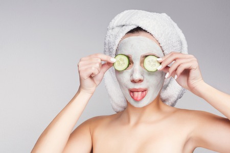 Beautiful girl with collagen mask and cucumber slices on eyes having fun against grey background, getting beauty treatment. Spa concept with copy spaceの写真素材