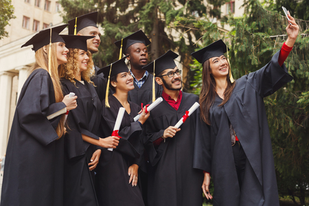 Group of multiethnic students taking selfie on smartphone to celebrate their graduation. Education, qualification and gown concept.の写真素材