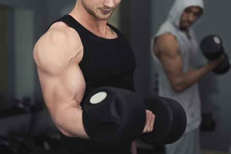 Young unrecognizable muscular bodybuilder doing heavy deadlifts in modern fitness center. Strong man exercising with dumbbells at gym, copy space, closeupの写真素材