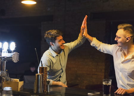 Old friends meeting. Two cheerful friends meet in beer pub, greeting each other with high five, copy spaceの写真素材