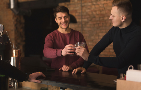 Friendly talk in bar. Top view of two happy young men talking to each other and enjoying whiskey, cheering at bar counter, copy spaceの写真素材