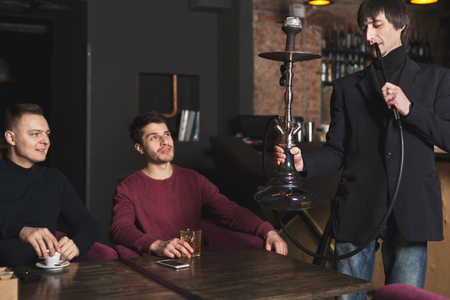 Two confident businessmen drinking whiskey and ordering hookah, having informal business meeting at...