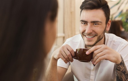 Handsome young man smiling, enjoying cup of coffee and having good time with his date in cafe, copy spaceの写真素材