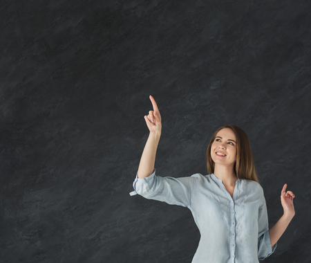 Woman working with virtual screen. Happy girl pointing on free space at gray backgroundの写真素材