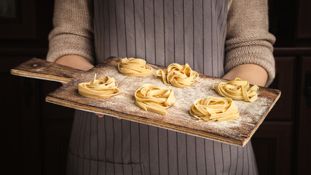 Woman chef holding wooden cutting board with yellow fettuccine nests on kitchenの写真素材