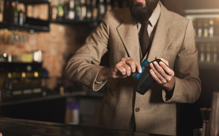Bartender making payment with credit card and POS-terminal, standing at bar counter, copy spaceの写真素材