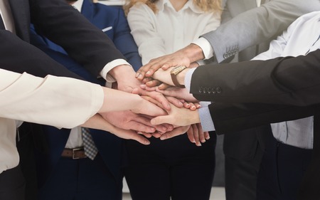 United coworkers standing with their hands together above workplace in modern office, celebrating successful project, teambuilding and unity backgroundの写真素材
