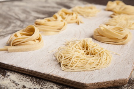 Raw tagliatelle nest on kitchen table. Preparing homemade Italian pasta, copy spaceの写真素材