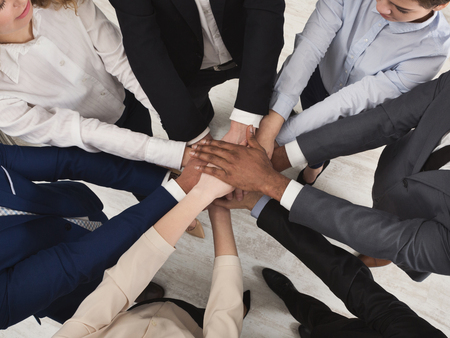 United coworkers standing with their hands together in modern office, celebrating victory, top view,...