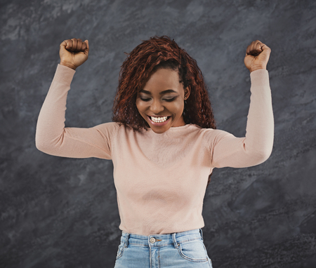 Excited young african american woman cheering with raised hands against grey backgroundの写真素材
