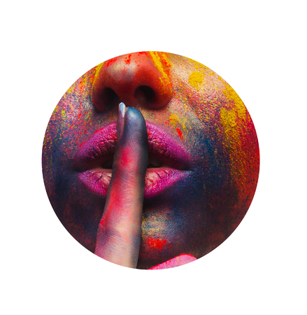 Beautiful girl with bright colorful art makeup closing her lips with finger. showing hush sign through round hole in white paper, copy spaceの写真素材