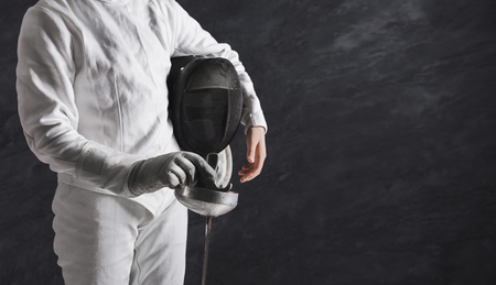 Fencer girl in fencing suit holding mask and sword at black background, crop, copy space