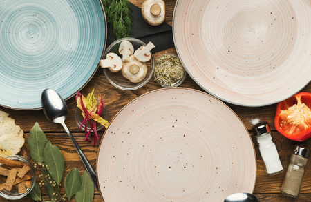 Set of three empty ceramic round plates on wooden table with food ingredients, mockup for meal, top viewの写真素材