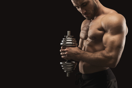 Athletic young man with dumbbell on black background, making strenth biceps exercises. Naked torso, muscular body, bodybuilding concept, copy spaceの写真素材