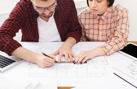 Two colleagues discussing architectural project, working with blueprints in modern workplace interior, copy space, closeupの写真素材