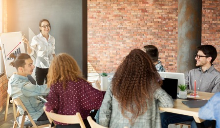 Cheerful woman top manager making presentation to colleagues, showing increasing financial chart on whiteboard, copy spaceの写真素材
