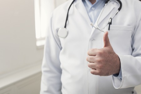 Unrecognizable doctor at his office. Male physician uniform at hospital showing thumb up gesture. Medicine and healthcare concept, copy spaceの写真素材