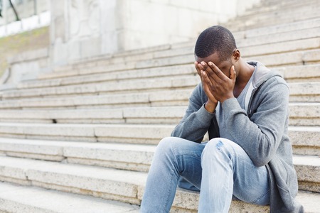 Desperate african-american student sitting on stairs outdoors in university campus. Man closed his face with his hands. Migraine, education and overworking concept, copy spaceの写真素材