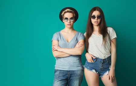 Trendy hipster girls in hats and glasses posing at blue background, copy spaceの写真素材