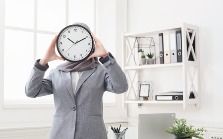 Arab woman covering face with office clock at workpalceの写真素材