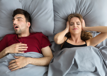 Snoring husband. Angry woman covering ears, top view in bed.