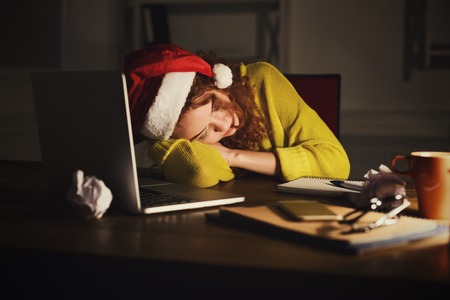Tired freelancer working on laptop on Christmas Eve. Woman in santa hat put her head on her hands while sitting at her working place working late on holiday evening, copy space, side viewの写真素材