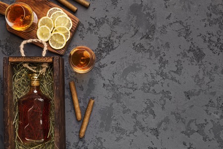 Bottle of aged brandy gift package shipping, two portions of drink, cigars and sliced lemon, black marble table, top view, copy spaceの写真素材