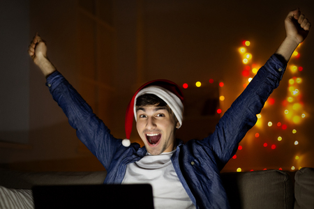 Happy new year! Happy man in santa hat with laptop at homeの写真素材