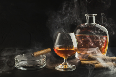 Glass of whiskey with smoking cigar and ibottle on black background, copy spaceの写真素材