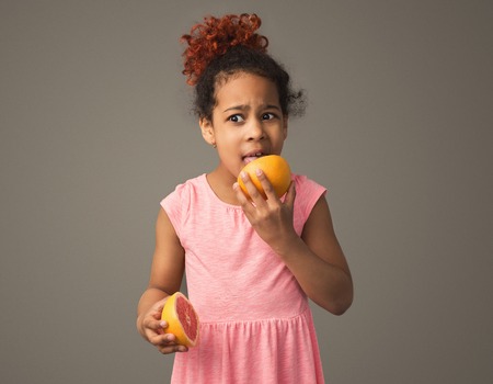 Little black girl eating grapefruit for the first time, studio shotの写真素材