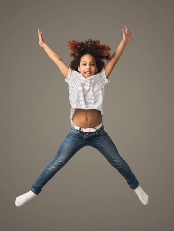 Beautiful little african-american girl jumping a gray studio background, copy space. Studio shot of cute happy childの写真素材