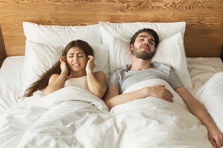 Snoring husband. Angry woman covering ears in bed.の写真素材