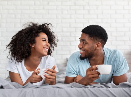 Happy african-american couple spending weekend morning together, drinking coffee in bed, copy spaceの写真素材