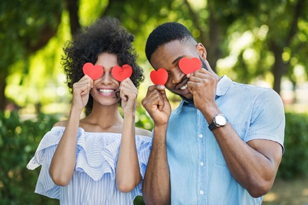 Happy african-american couple with paper hearts in park on sunny dayの写真素材